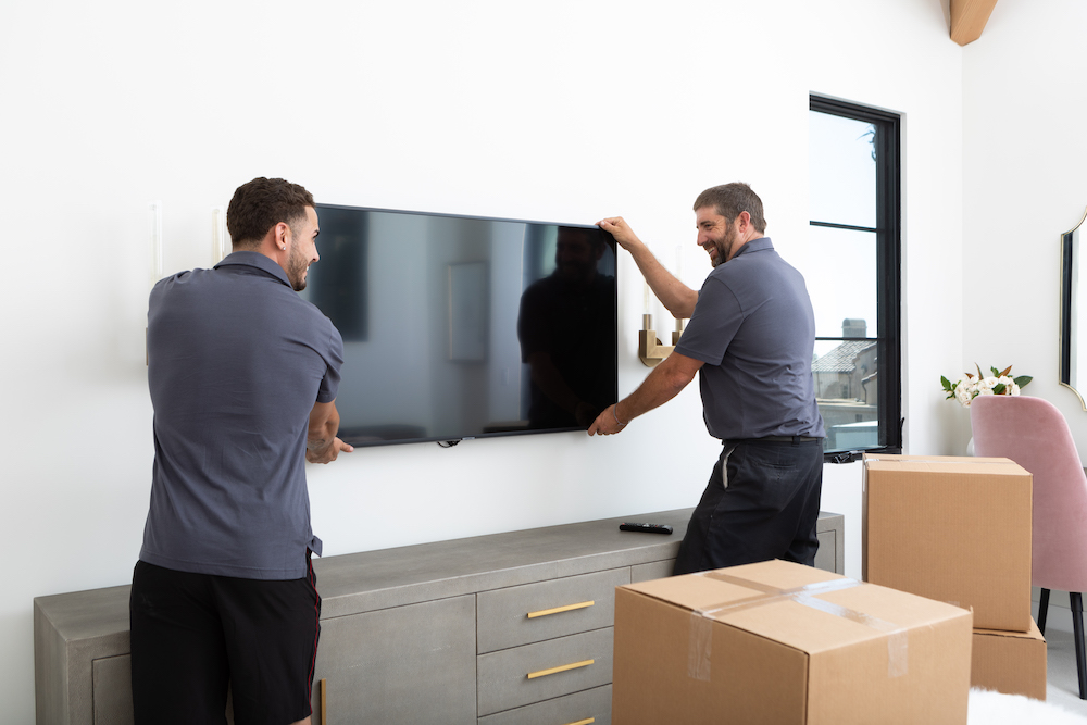Movers carefully hanging a television on the wall